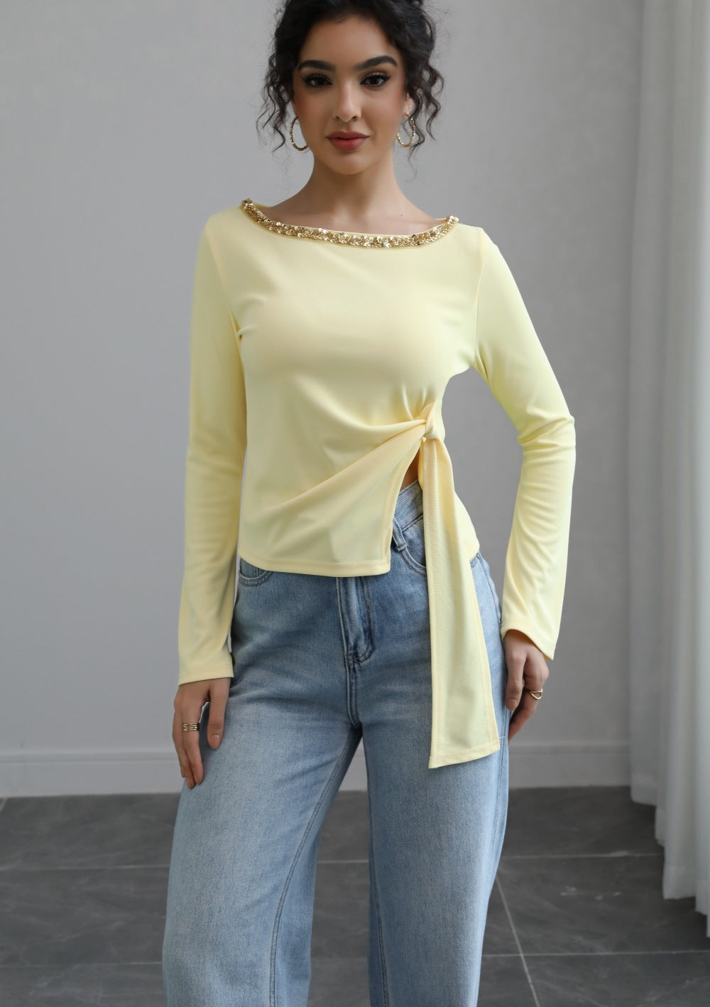 Malbusaat model wearing pale yellow autumn lace up top with jewelled neckline and side tie over blue jeans