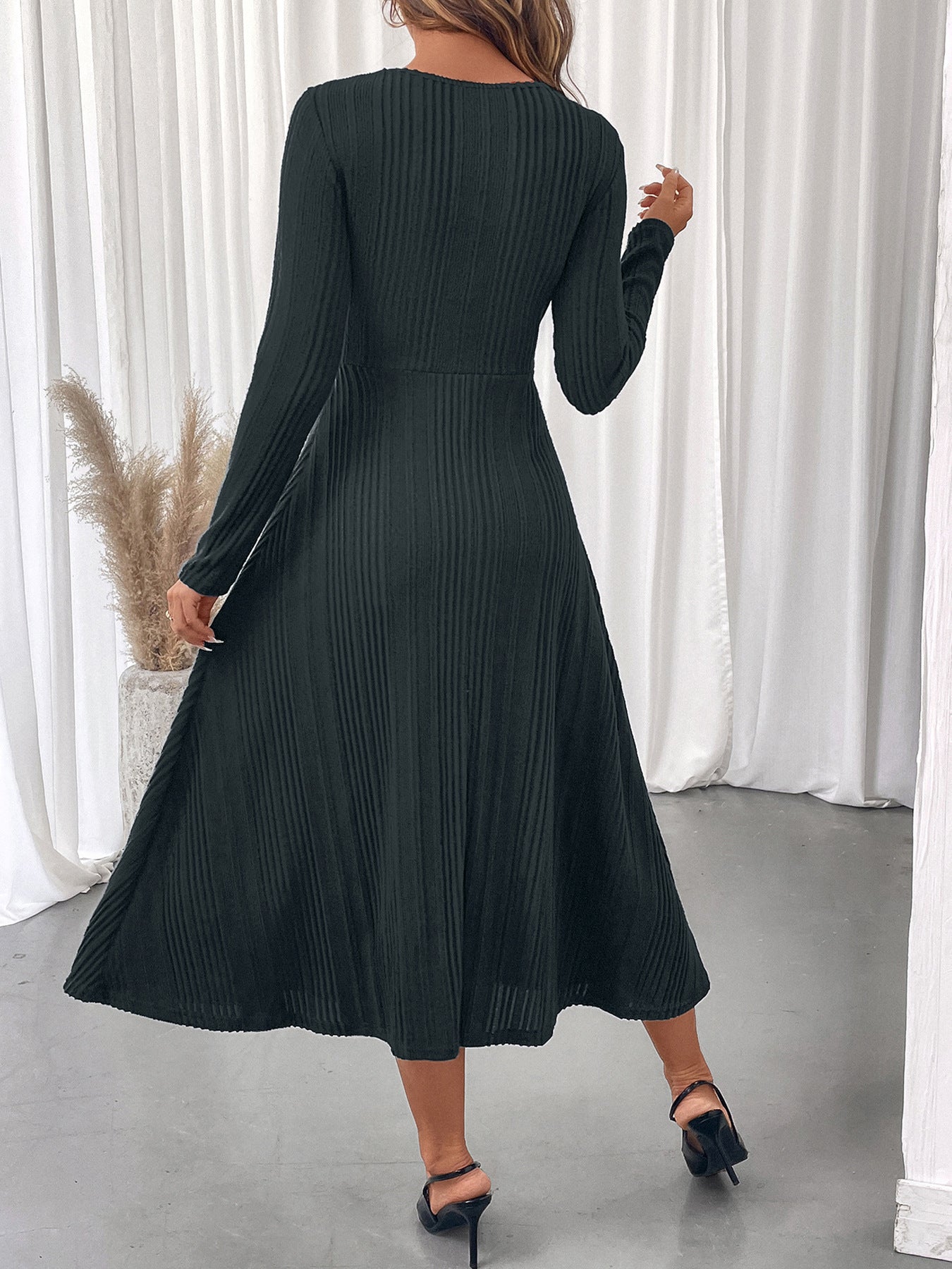 Back view of a black autumn slim fit midi dress with long sleeves worn with black heels