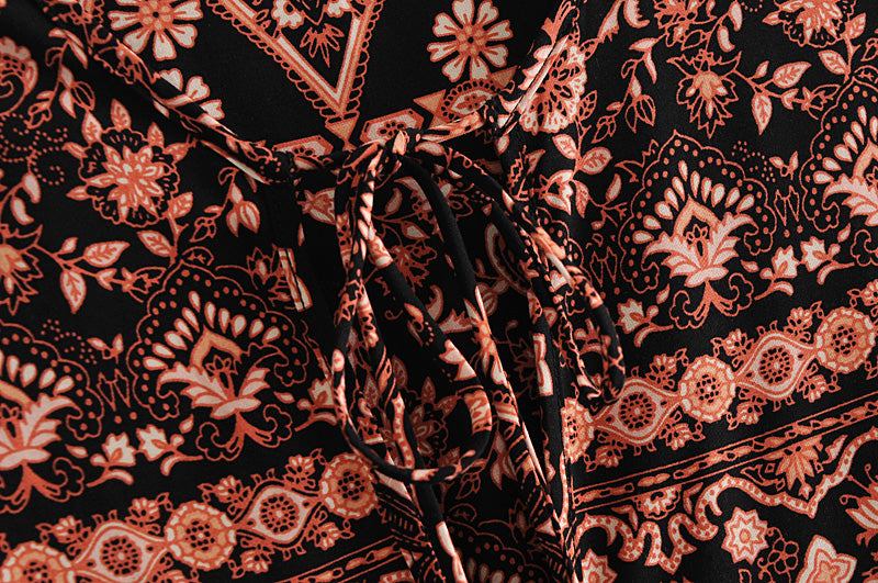 Close-up of Malbusaat loose fit printed holiday dress fabric with intricate floral and geometric patterns in black and orange