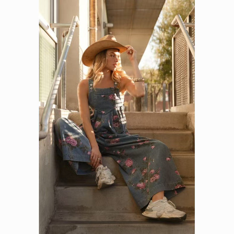 Casual floral denim jumpsuit for women, styled with a hat and sneakers, sitting on outdoor stairs