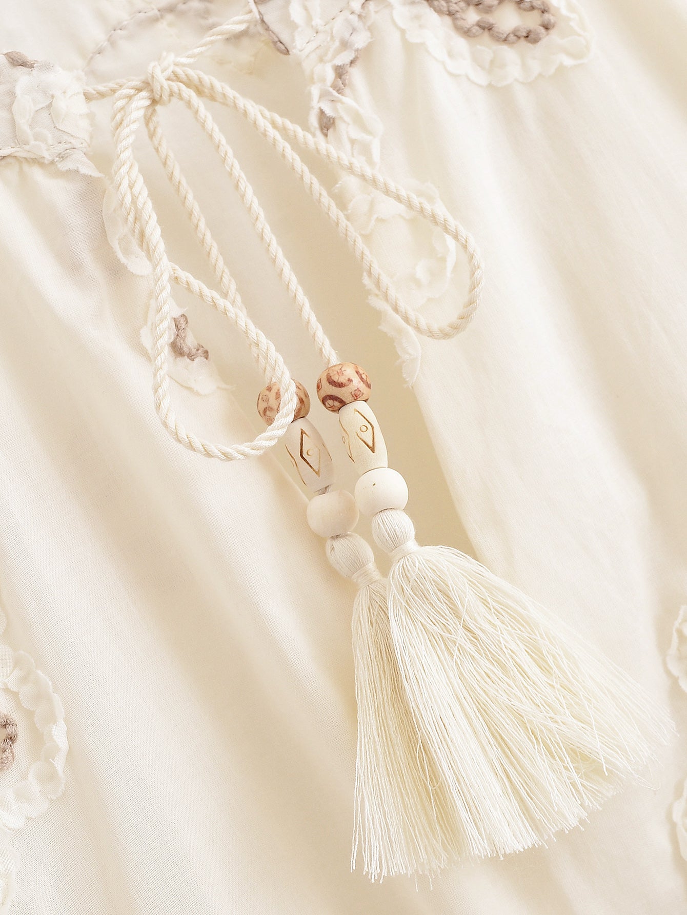 Close-up of tassel and embroidered details on a Malbusaat floral mini shirt for women in cream fabric
