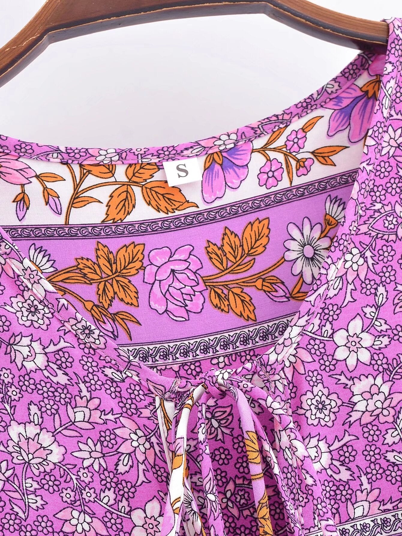 Close-up of Malbusaat floral tie-neck maxi dress with purple and orange flower pattern on hanger