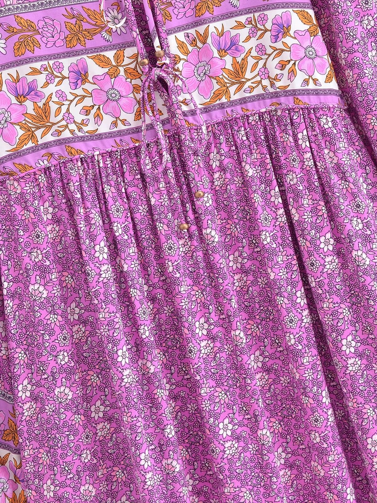 Close-up of a pink and purple floral tie-neck maxi dress with detailed flower patterns and a tie neckline