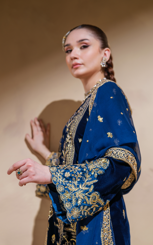 Elegant model showcasing a midnight blue velvet Pakistani suit with intricate gold embroidery