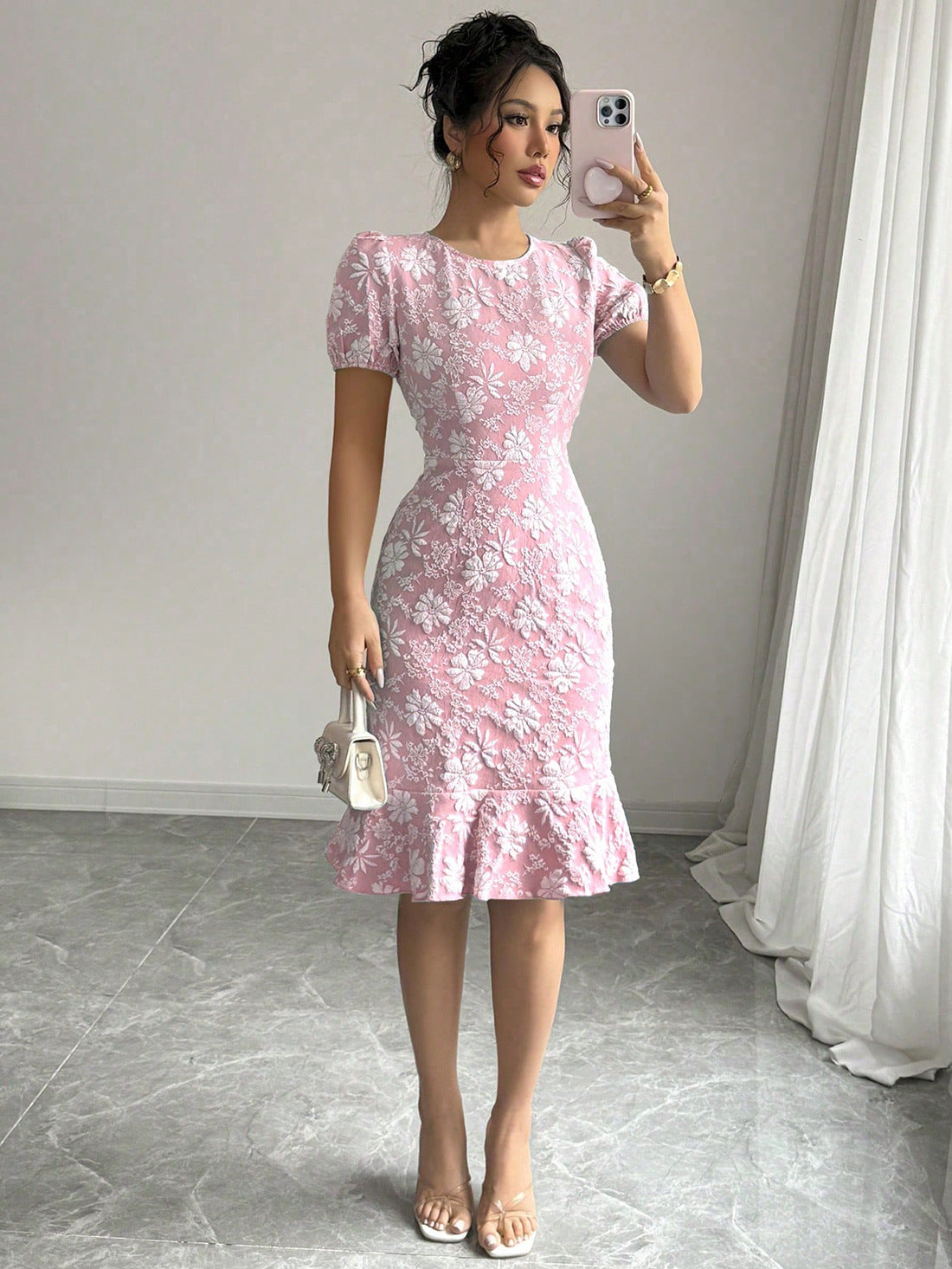 Woman wearing pink floral fishtail bodycon dress with puff sleeves and ruffled hem holding a white handbag