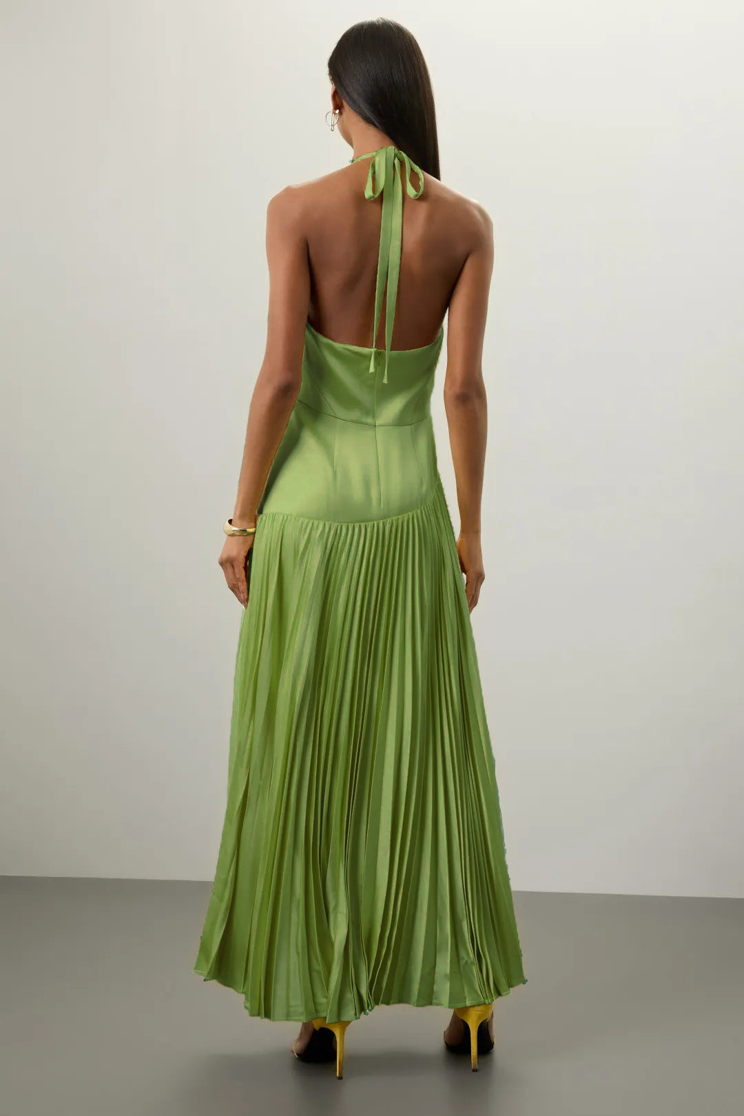 Back view of model wearing green pleated halter dress for summer by Malbusaat with flowing skirt