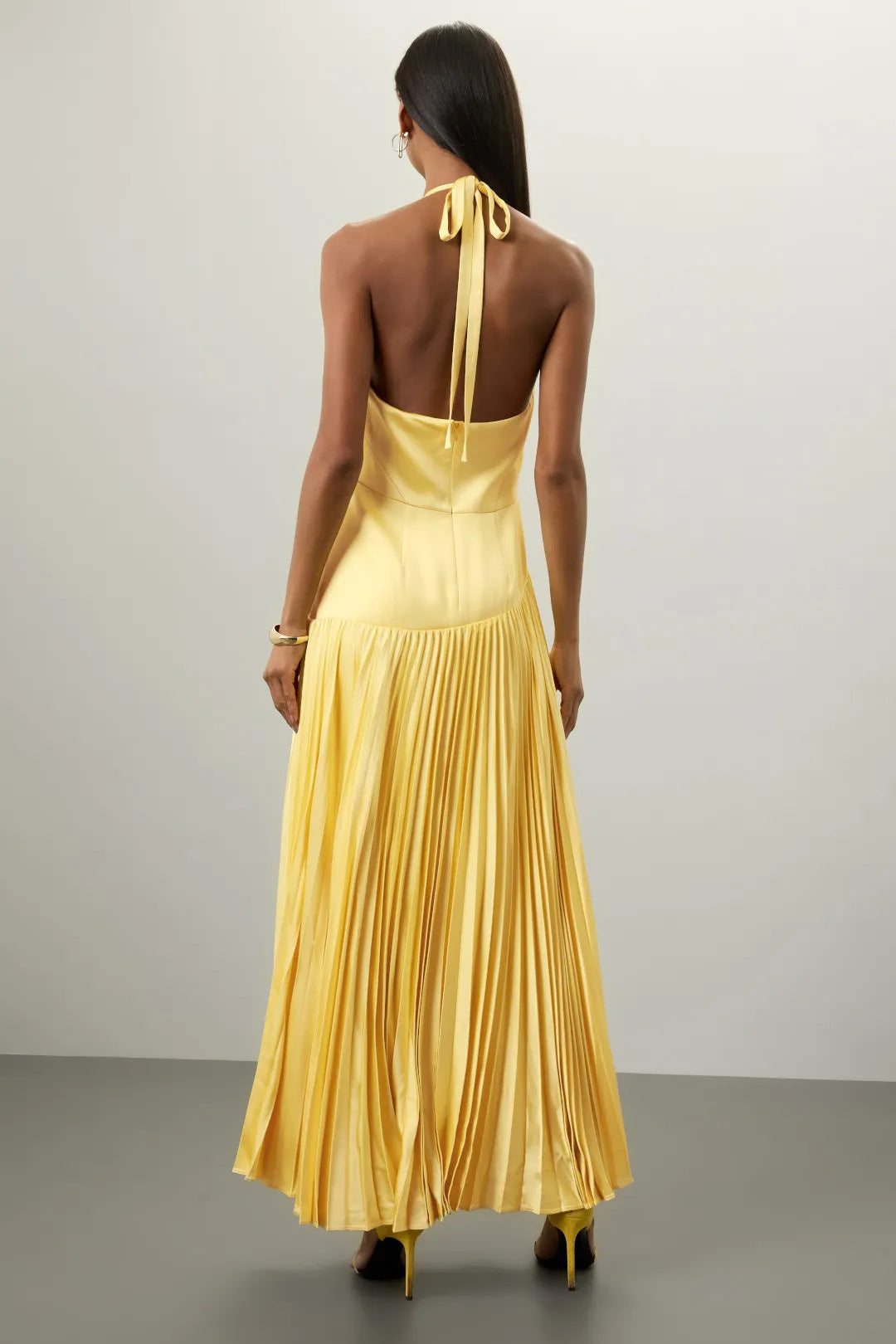 Back view of yellow pleated halter dress for summer with tie neck and flowing skirt by Malbusaat