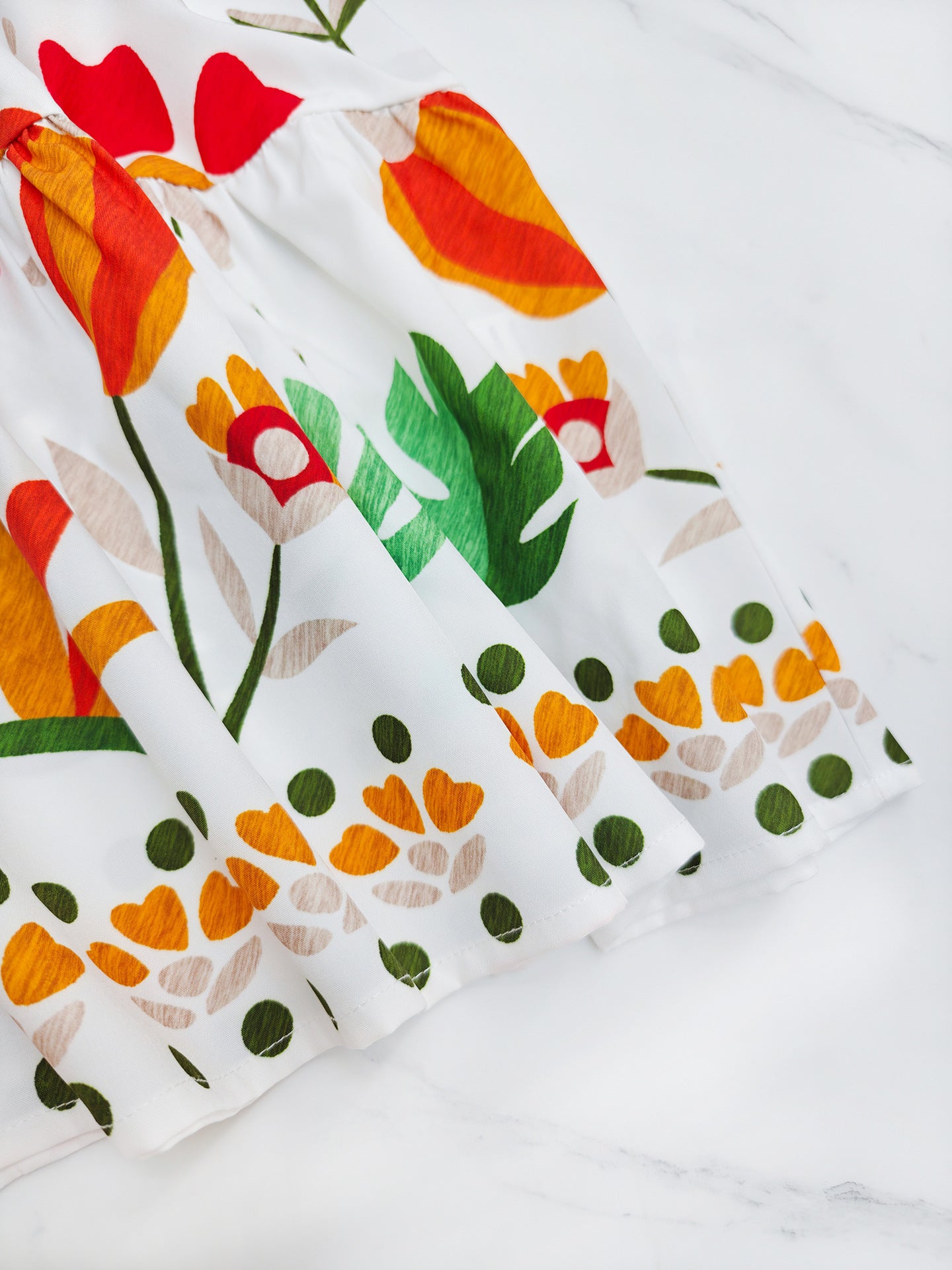 Close-up of a Malbusaat printed strap tiered dress featuring vibrant floral patterns in red, yellow, and green