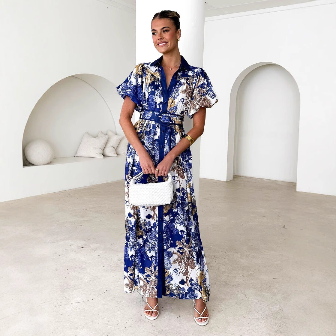 Woman wearing blue and beige floral stand collar ruffle top dress with a belt and white handbag