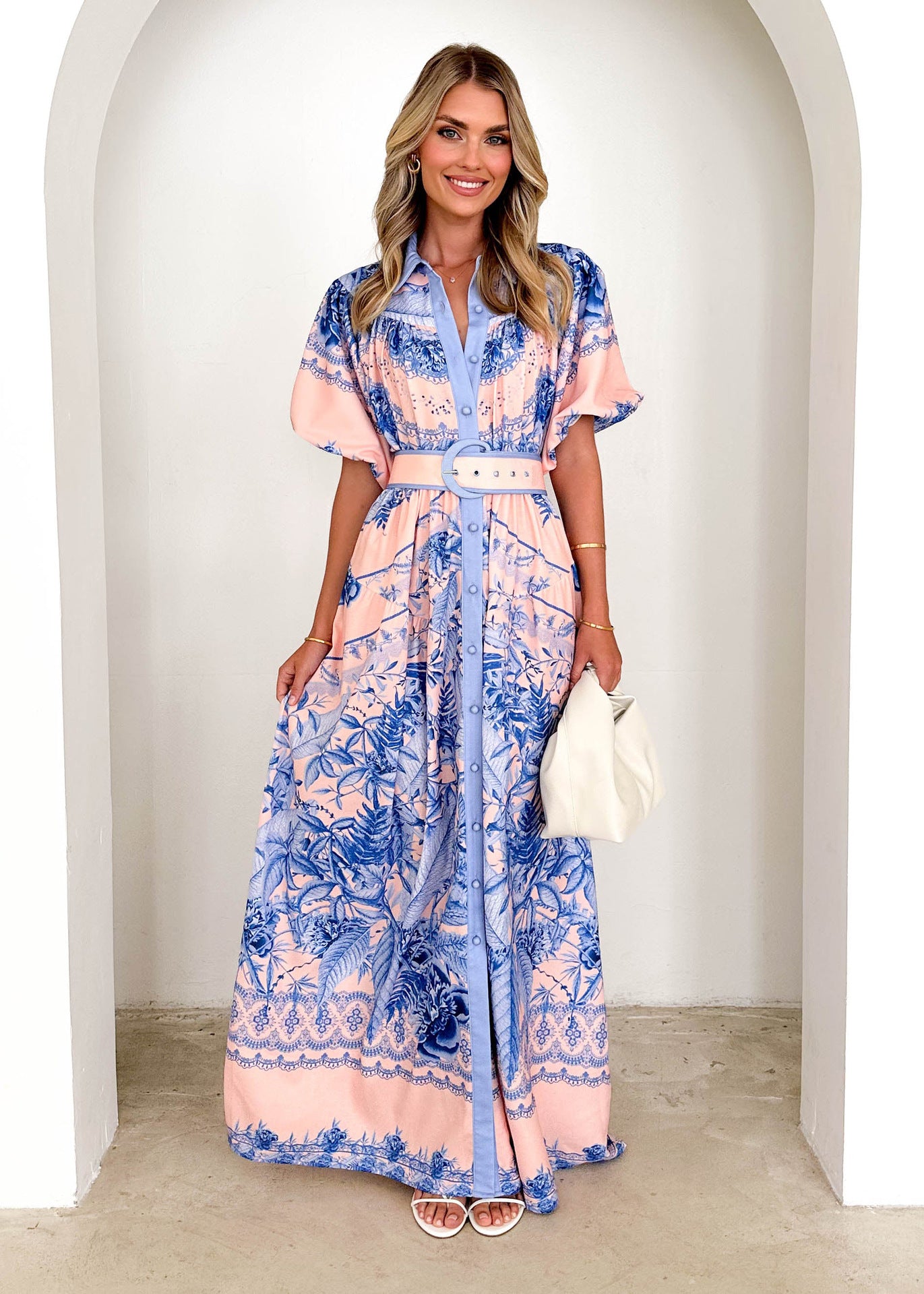Woman wearing a Malbusaat stand collar ruffle top dress with blue and peach floral print and belted waist