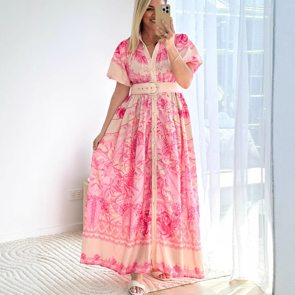 Woman wearing a pink floral stand collar ruffle top dress with a belt standing by a window