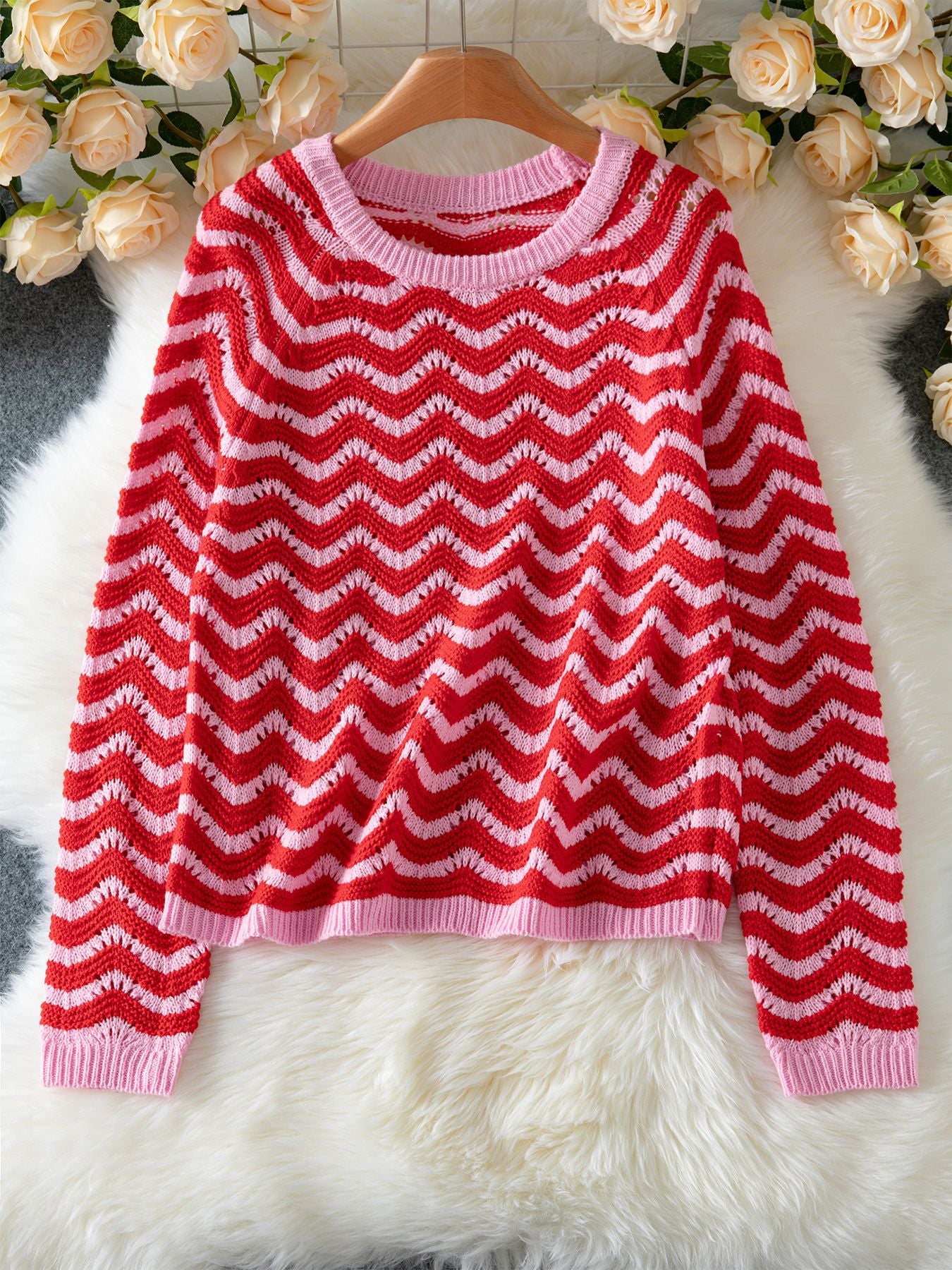 Red and pink striped knit sweater for women displayed on a wooden hanger with floral background